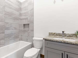 This modern bathroom features a sleek bathtub with marble-look tile surround and a convenient built-in niche.