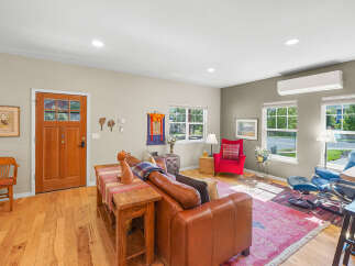 Step into this inviting living room featuring a warm leather sofa, a vibrant red accent chair, and a cozy rug perfect for relaxation.
