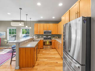 This modern kitchen boasts sleek stainless steel appliances, including a French door refrigerator and a gas range, complemented by warm wood cabinetry and a durable quartz countertop.