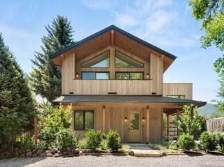 Experience modern mountain living in this stunning wood-clad home, featuring a striking asymmetrical roofline and expansive triangular windows that flood the interior with natural light.