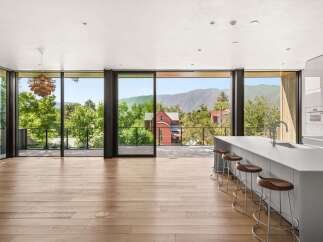 Experience breathtaking mountain views from this modern kitchen, featuring a sleek island with bar seating and expansive floor-to-ceiling windows.