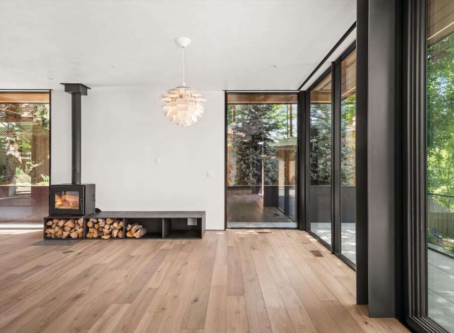 Experience modern living in this stunning home featuring a sleek black wood-burning stove and ample firewood storage, perfect for cozy evenings.