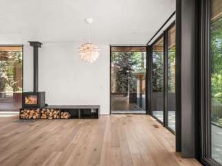 Experience modern living in this stunning home featuring a sleek black wood-burning stove and ample firewood storage, perfect for cozy evenings.