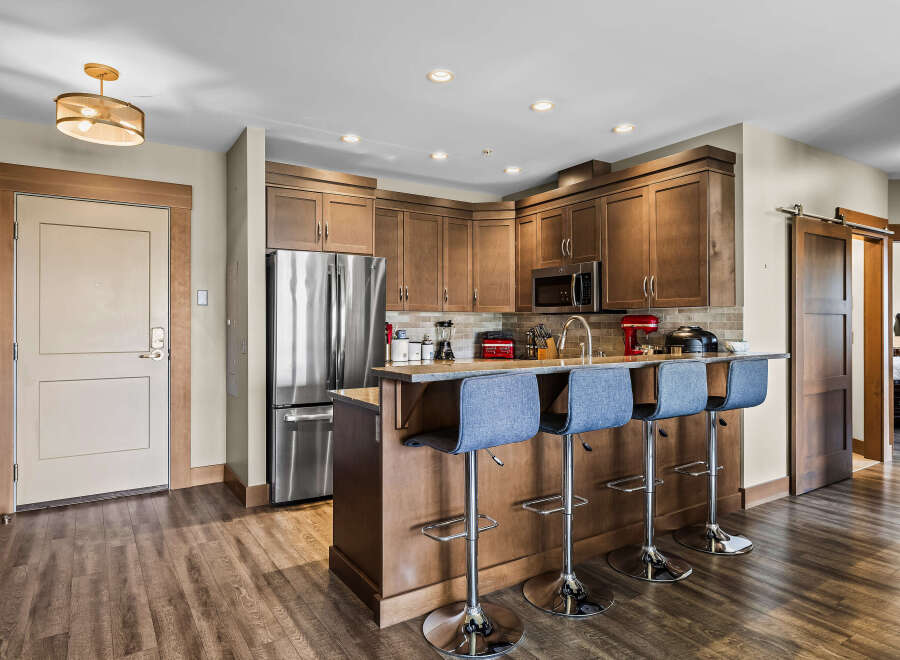 This modern kitchen features rich wood cabinetry, a sleek stainless steel refrigerator, and a convenient breakfast bar with comfortable seating.