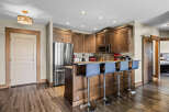 This modern kitchen features rich wood cabinetry, a sleek stainless steel refrigerator, and a convenient breakfast bar with comfortable seating.