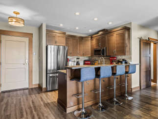 This modern kitchen features rich wood cabinetry, a sleek stainless steel refrigerator, and a convenient breakfast bar with comfortable seating.