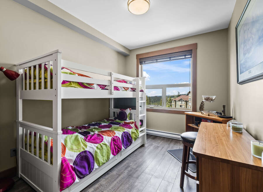 This charming bedroom features a white bunk bed with vibrant, colorful bedding, perfect for accommodating guests or children.