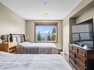 Experience breathtaking mountain views from this stunning bedroom, featuring two comfortable beds and a large window overlooking a serene landscape.