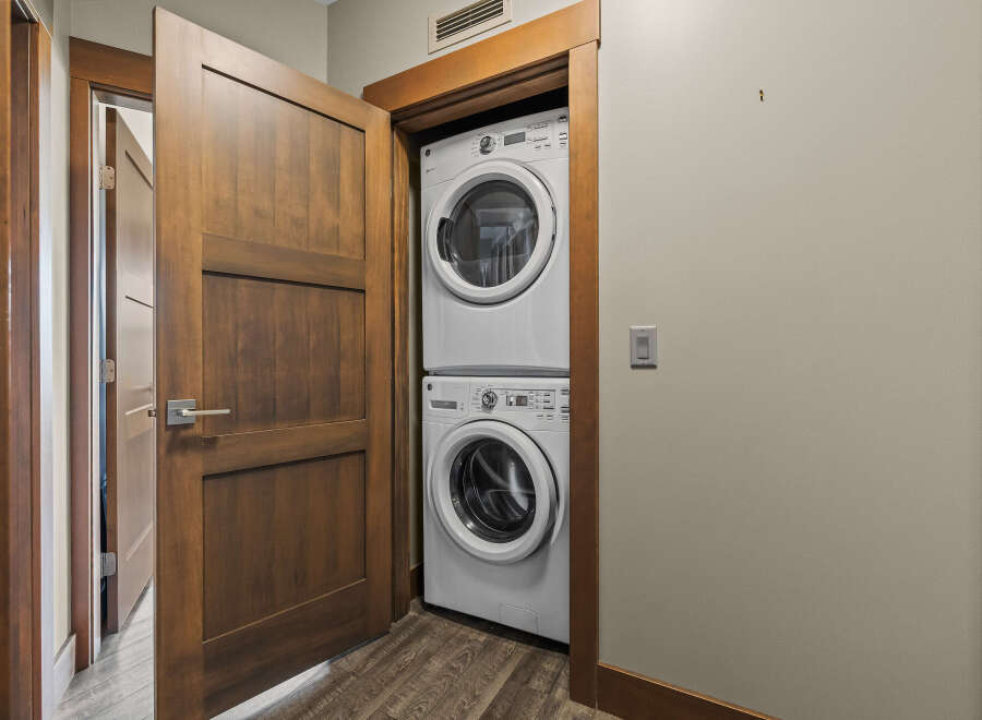 Discover the convenience of in-suite laundry with this stacked GE washer and dryer set, neatly tucked away behind a stylish wooden door.