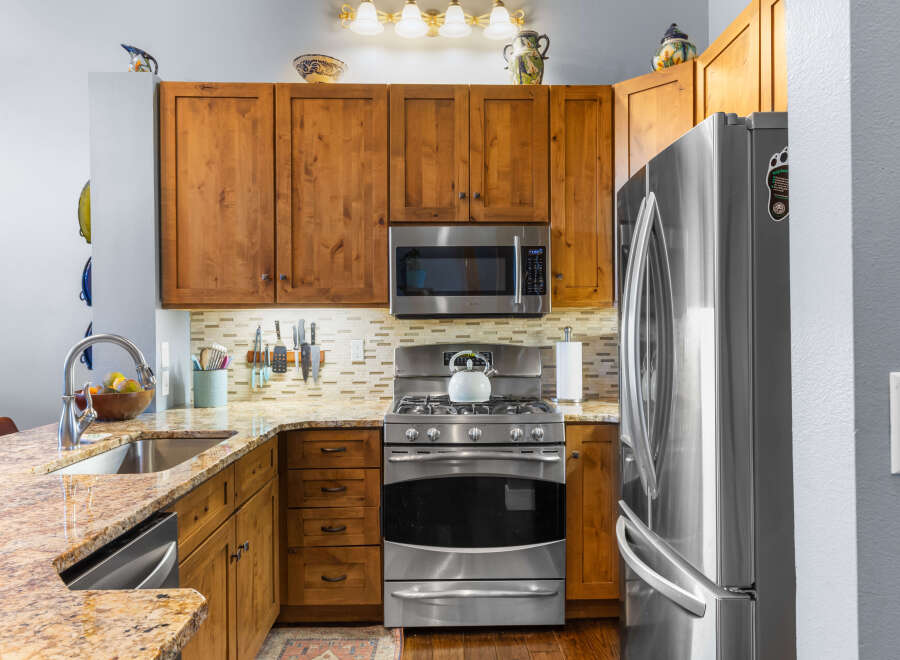 This kitchen boasts beautiful natural wood cabinetry, complemented by a sleek stainless steel appliance suite including a microwave, gas range, and refrigerator.