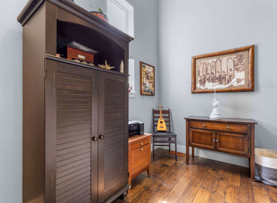This charming room features a large dark wood armoire providing ample storage, complemented by a vintage-style wooden desk and a decorative framed photograph.