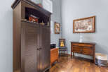 This charming room features a large dark wood armoire providing ample storage, complemented by a vintage-style wooden desk and a decorative framed photograph.