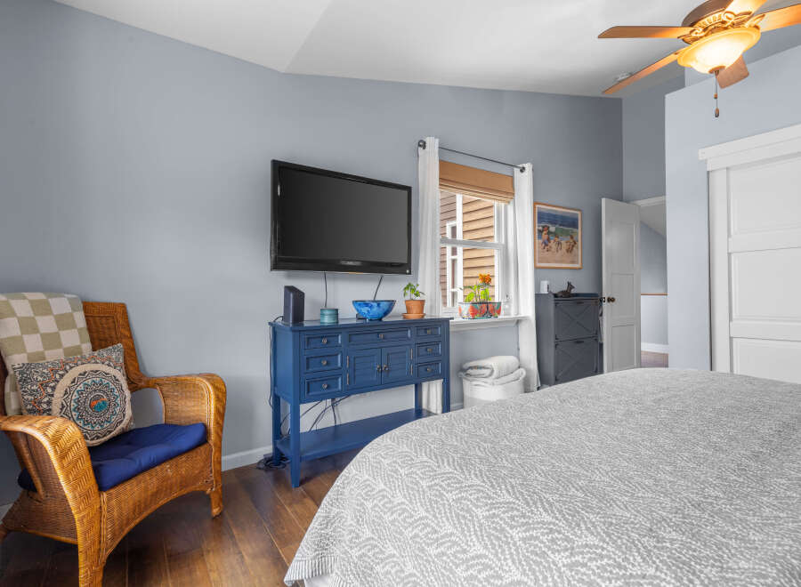 This cozy bedroom features a comfortable wicker chair with decorative pillows and a checkered throw, perfect for relaxing.
