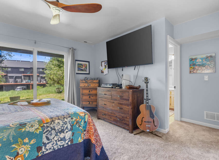 This inviting bedroom features a comfortable bed with a vibrant, patchwork quilt and a large sliding glass door offering scenic views of the outdoors.