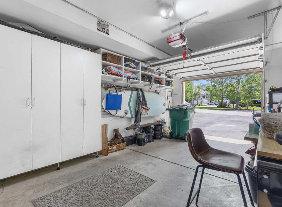 Discover ample storage solutions in this spacious garage, featuring tall white cabinets and open shelving perfect for organizing all your tools and recreational gear.