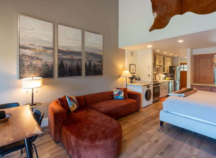 Experience cozy living in this studio apartment featuring a plush, rust-colored sectional sofa and a comfortable bed.