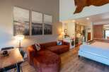 Experience cozy living in this studio apartment featuring a plush, rust-colored sectional sofa and a comfortable bed.
