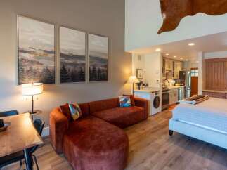Experience cozy living in this studio apartment featuring a plush, rust-colored sectional sofa and a comfortable bed.