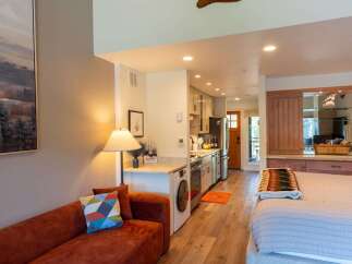 Discover this charming studio apartment featuring a cozy living area with a plush sofa and a vibrant accent pillow.
