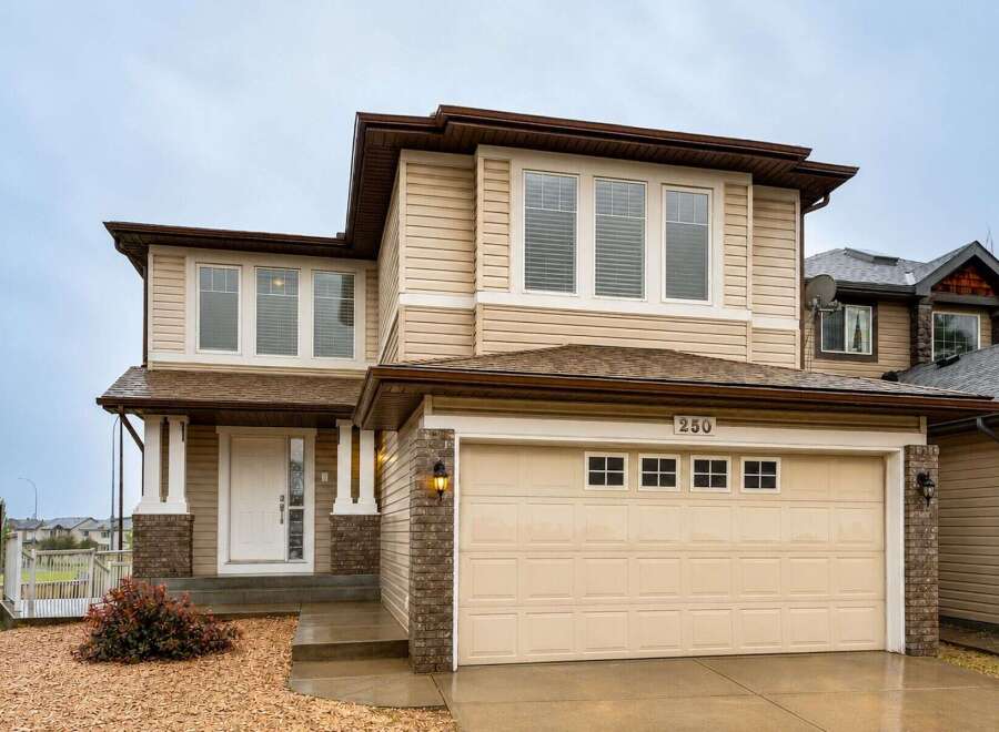 This charming two-story home features a welcoming covered porch with brick accents and a spacious attached garage.