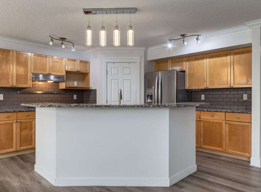 This spacious kitchen features beautiful light wood cabinetry complemented by a dark subway tile backsplash and granite countertops.