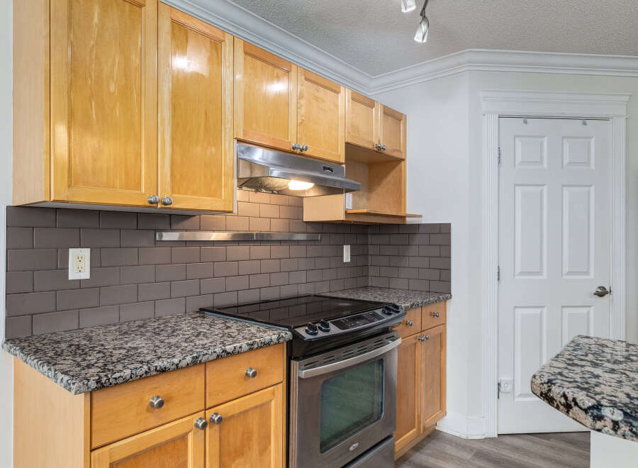 This kitchen features warm, honey-toned wood cabinets complemented by sleek, dark subway tile backsplash and granite countertops.