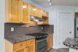 This kitchen features warm, honey-toned wood cabinets complemented by sleek, dark subway tile backsplash and granite countertops.