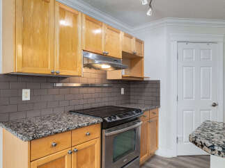 This kitchen features warm, honey-toned wood cabinets complemented by sleek, dark subway tile backsplash and granite countertops.