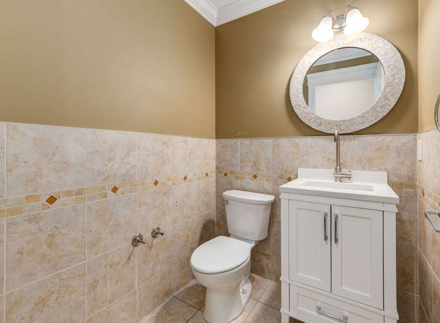 This bathroom features a modern white vanity with chrome hardware, complemented by a stylish round mirror with a mosaic frame.