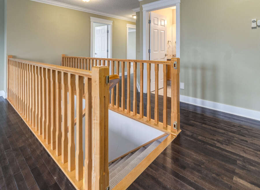 This image showcases a beautifully designed hallway with a wooden banister and dark hardwood floors.