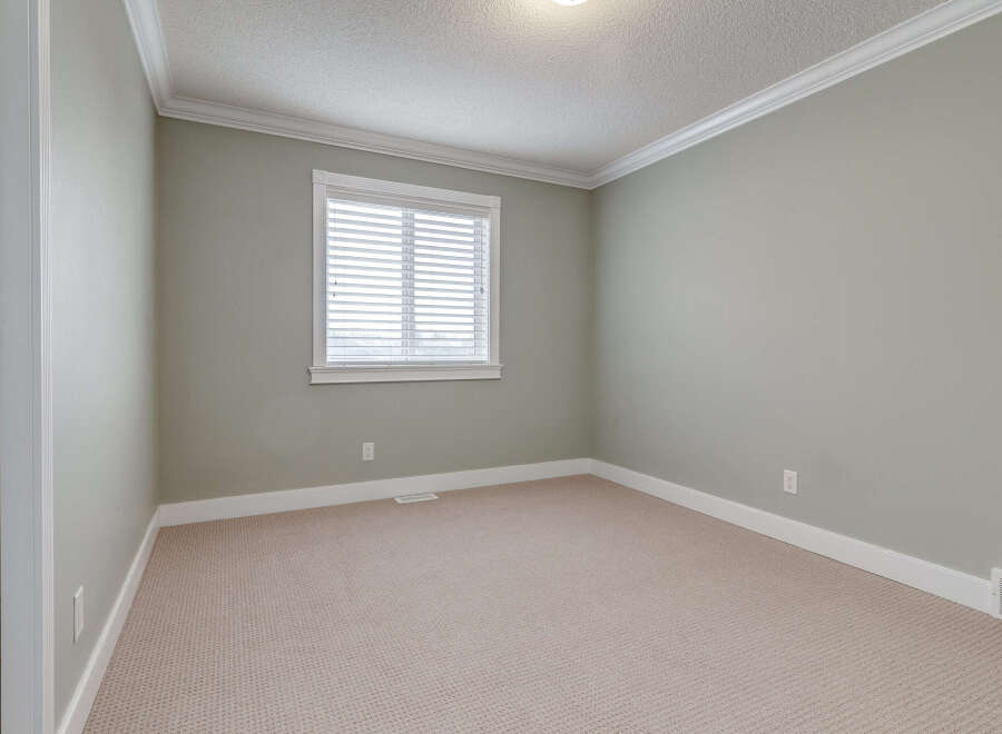 This empty room features a neutral color palette with light gray walls and a beige carpeted floor, creating a versatile canvas for any decor style.