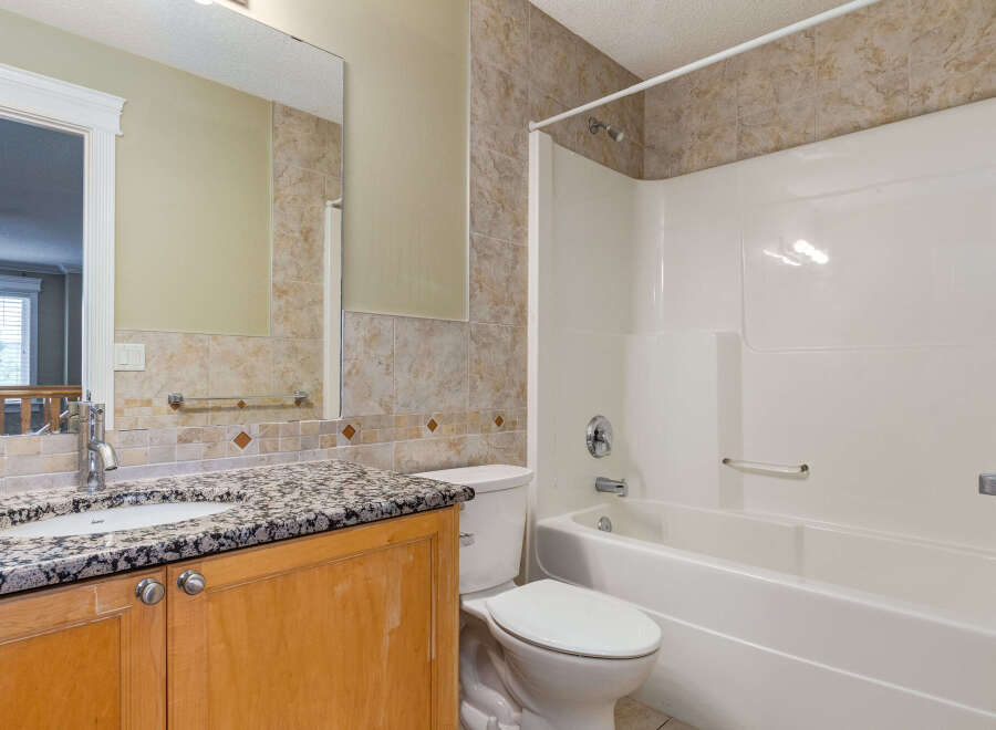 This bathroom features a granite countertop vanity with a single sink and wooden cabinets, complemented by a tiled backsplash.
