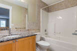 This bathroom features a granite countertop vanity with a single sink and wooden cabinets, complemented by a tiled backsplash.