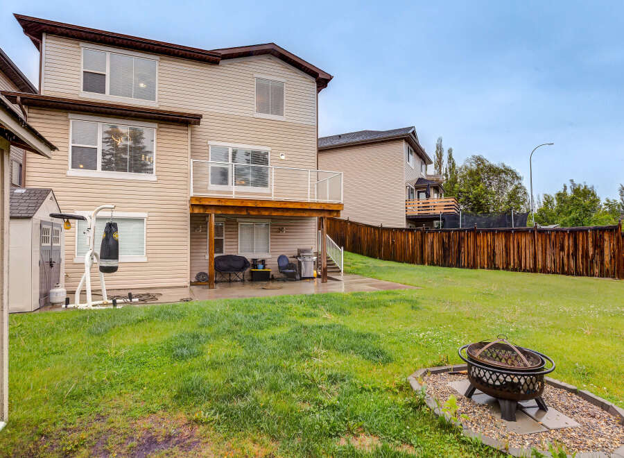 Enjoy outdoor living in this spacious backyard featuring a wooden deck, a covered patio with a grill, and a fire pit for cozy evenings.