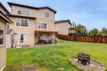 Enjoy outdoor living in this spacious backyard featuring a wooden deck, a covered patio with a grill, and a fire pit for cozy evenings.