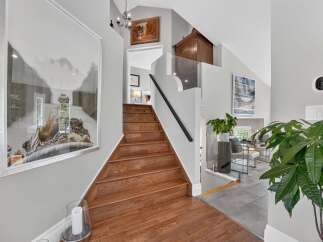 This stunning entryway features a grand wooden staircase leading to the upper level, complemented by a large framed artwork on the left wall.