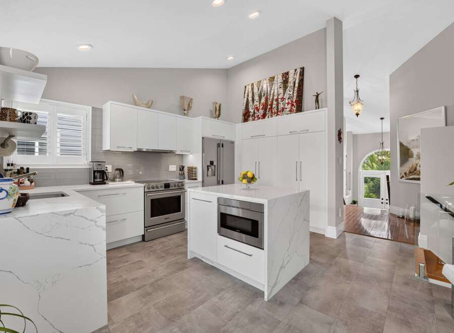 Experience modern luxury in this stunning kitchen featuring sleek white cabinetry, elegant marble countertops, and a central island with a built-in microwave.