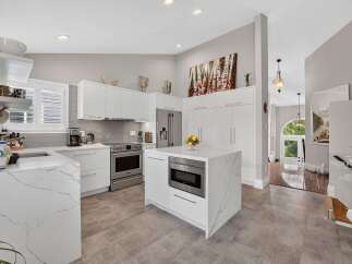 Experience modern luxury in this stunning kitchen featuring sleek white cabinetry, elegant marble countertops, and a central island with a built-in microwave.