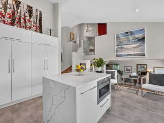 Experience modern living in this stunning kitchen featuring a sleek white island with a marble countertop and integrated microwave.
