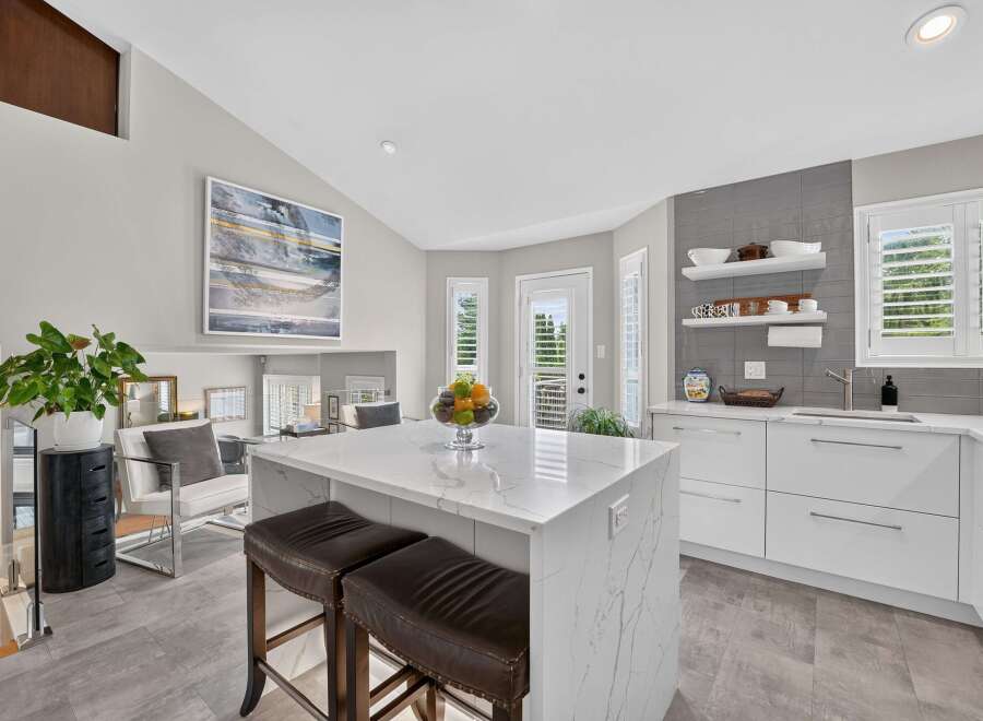 Experience modern luxury in this stunning kitchen, featuring a sleek white island with marble countertops and comfortable bar stools.