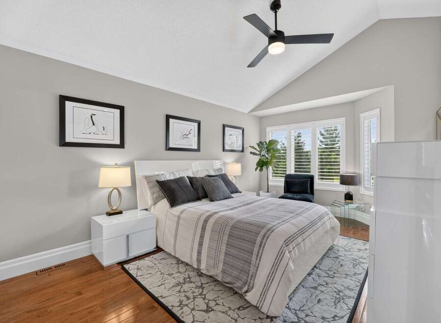 Experience luxury in this master bedroom, featuring a vaulted ceiling with a modern ceiling fan and ample natural light from the large windows.