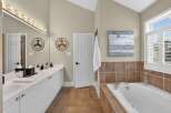 This spacious bathroom features a double vanity with ample counter space and storage, complemented by a large mirror and vanity lighting.