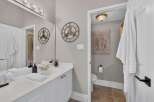This elegant bathroom features a spacious vanity with a white countertop and gold-accented fixtures, complemented by a large mirror reflecting a stylish wall clock.