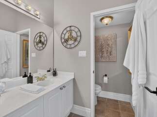 This elegant bathroom features a spacious vanity with a white countertop and gold-accented fixtures, complemented by a large mirror reflecting a stylish wall clock.