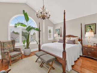 Experience luxury and comfort in this stunning master bedroom, featuring a grand four-poster bed and a beautiful arched window that floods the space with natural light.