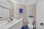This bright and airy bathroom features a spacious vanity with a double sink and elegant gold fixtures, complemented by a large mirror with vanity lighting.