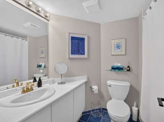 This bright and airy bathroom features a spacious vanity with a double sink and elegant gold fixtures, complemented by a large mirror with vanity lighting.
