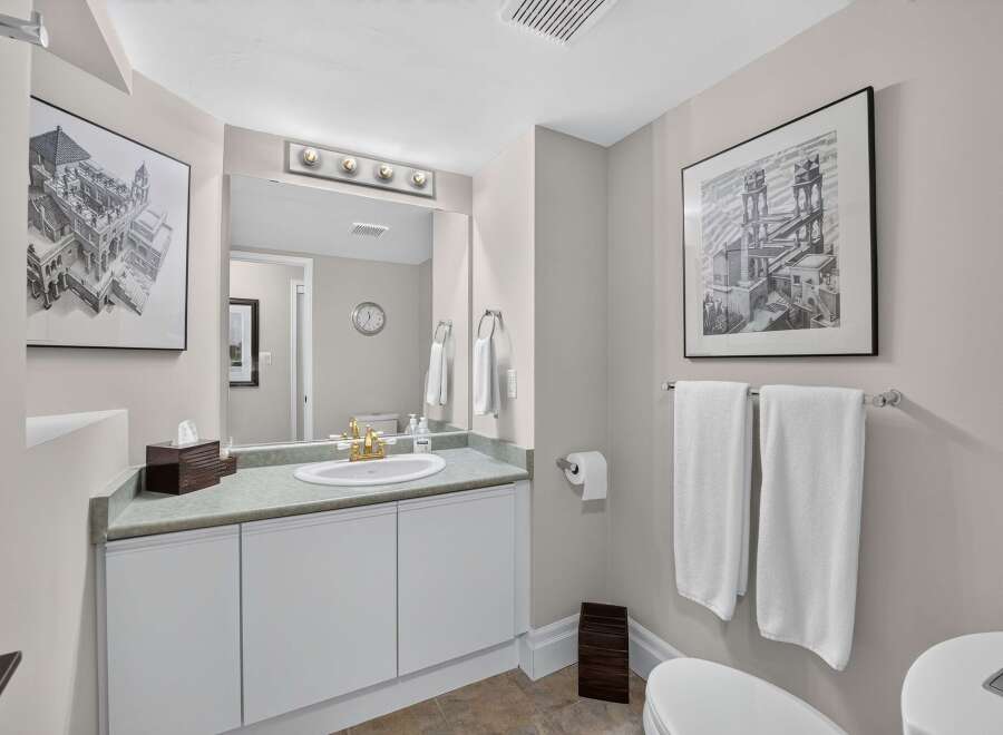 This elegant bathroom features a spacious vanity with a granite countertop and a gold-accented faucet, complemented by a large mirror with a vanity light fixture.