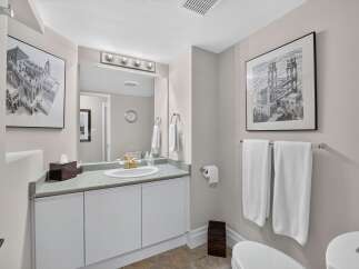 This elegant bathroom features a spacious vanity with a granite countertop and a gold-accented faucet, complemented by a large mirror with a vanity light fixture.