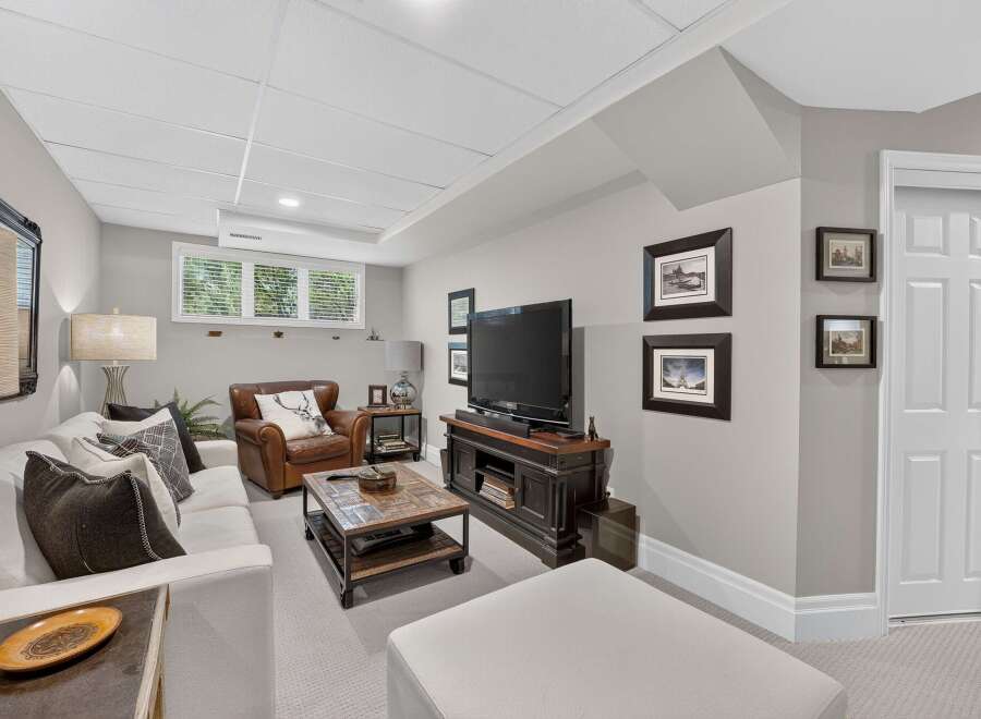 This inviting basement living area features a comfortable white sectional sofa paired with a rich leather armchair, perfect for relaxation.